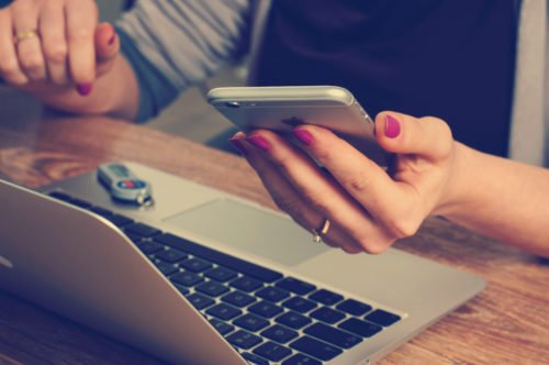 Service im digitalen Zeitalter: Frau mit Smartphone in der Hand sitzt vor einem Laptop